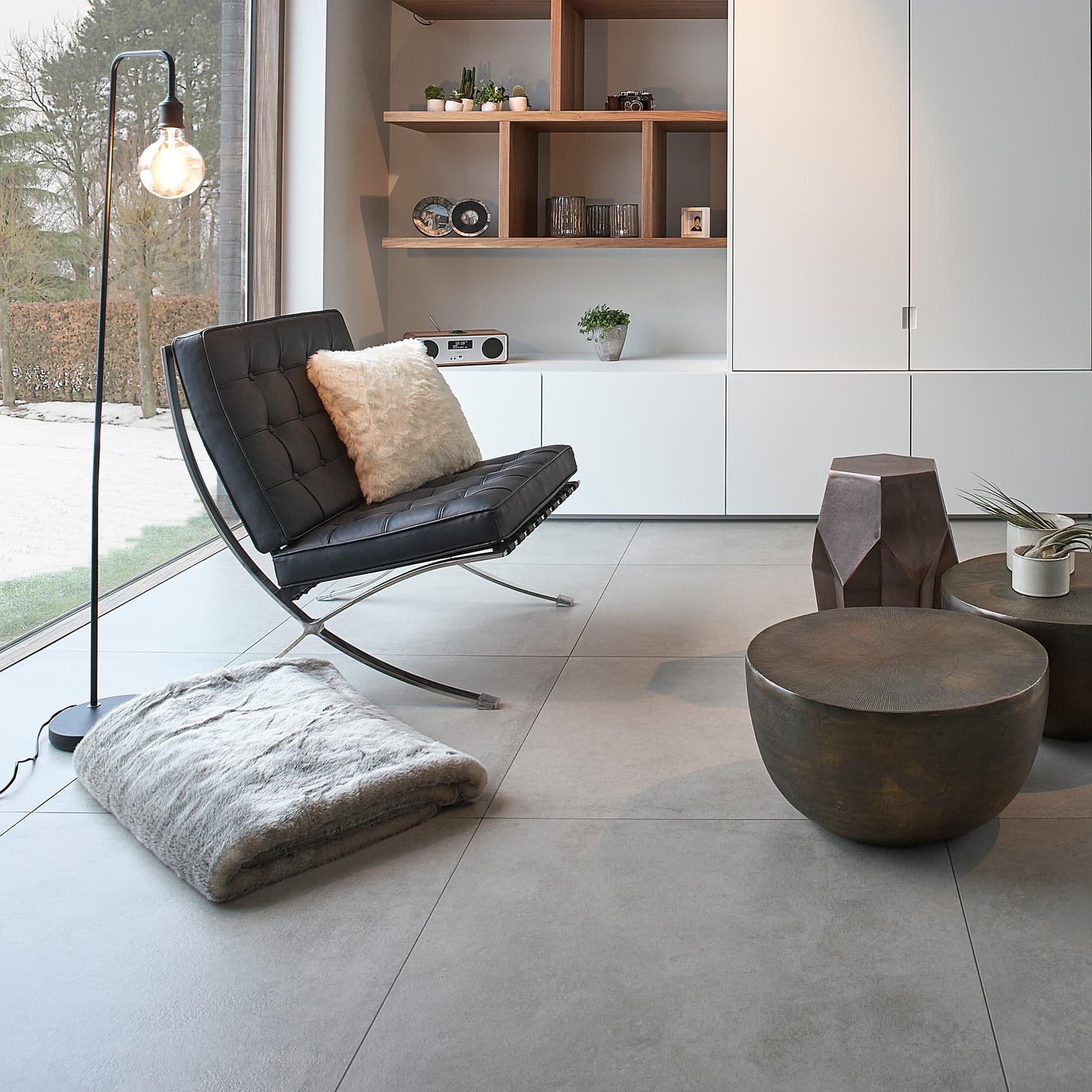 Stue med grå betongfliser på gulv, en sort designerlenestol, puff og kaffebord.
