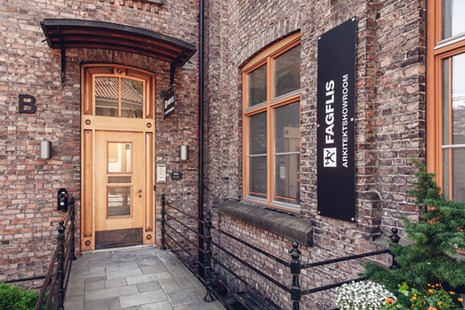 Inngangsparti og fasade ved FagFlis Arkitektshowroom på Sagene. Teglstein på vegger og gultonet dør i treverk.