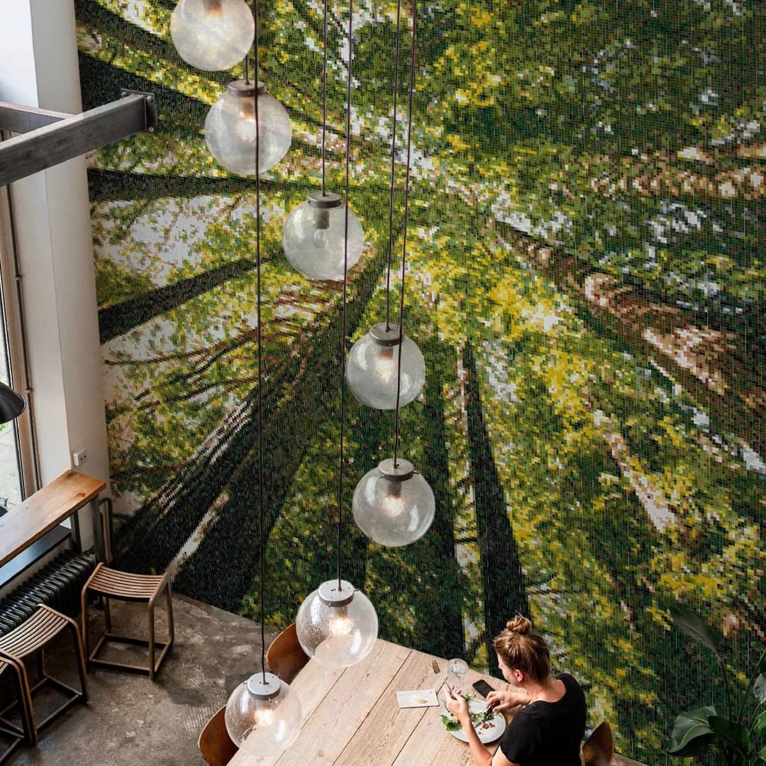 Vegg med fotorealistisk kunst laget av glassmosaikk. Kunsten viser en skog sett fra bunnen mot tretoppene